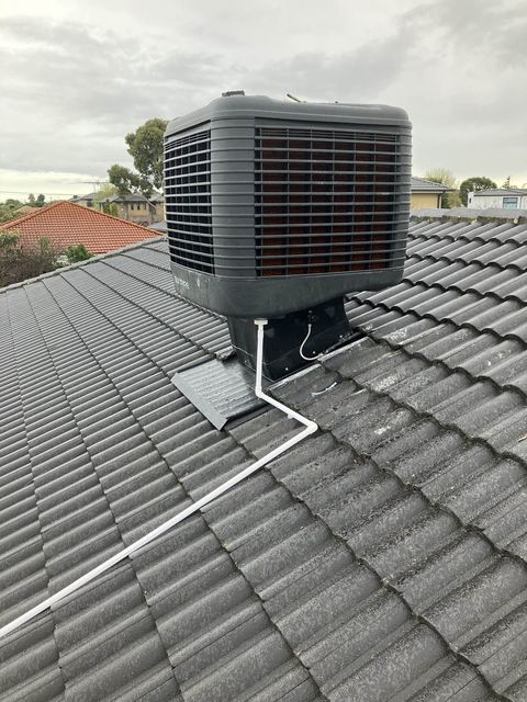 An evaporative cooler on a tiled roof, with its conduit run down the roof