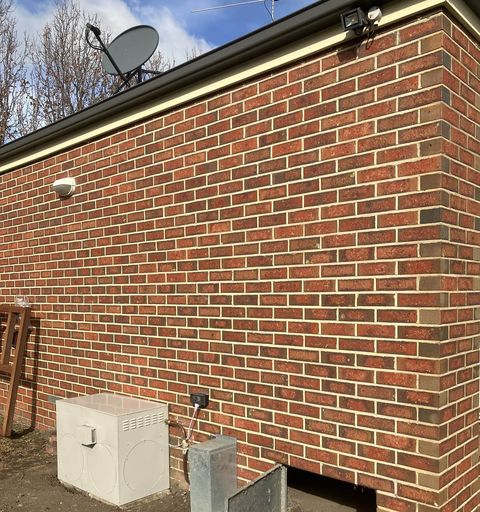 A gas ducted heater against a brick wall, beside the underfloor access