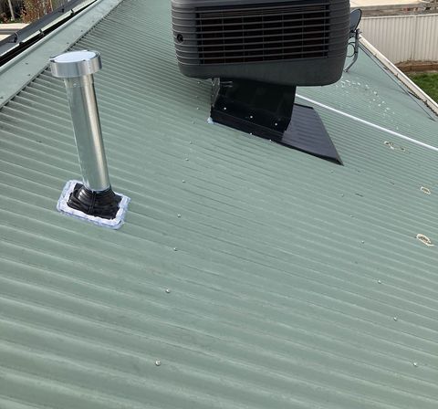 An evaporative cooler beside a new flue on a Colorbond roof
